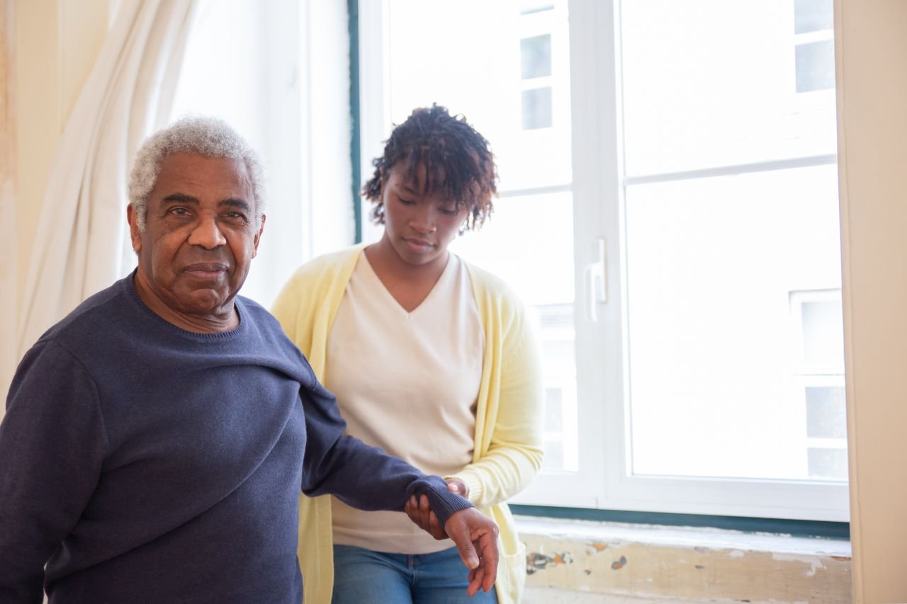 who-we-are An elderly man receives care from a young woman near a bright window in Portugal.